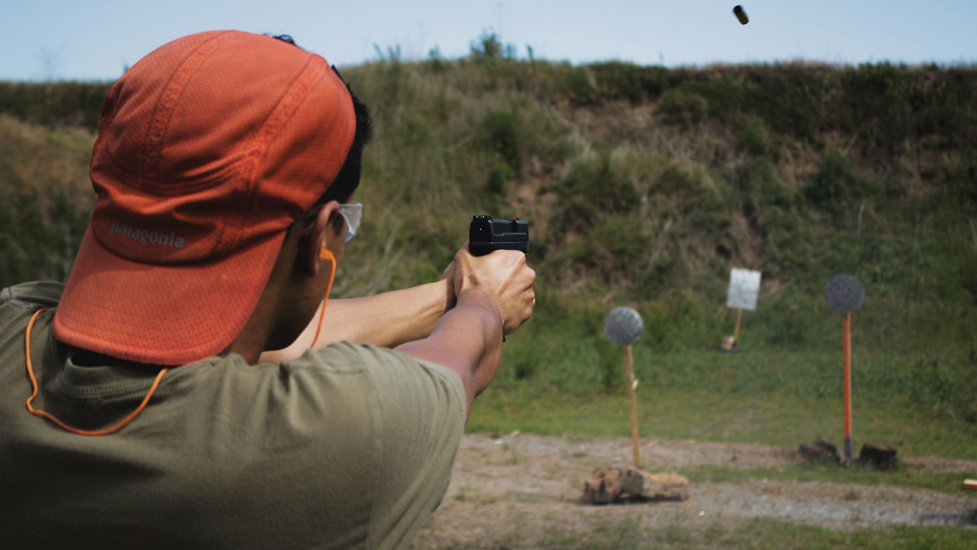 Tirador con gorra y gafas de protección disparando en un campo de tiro