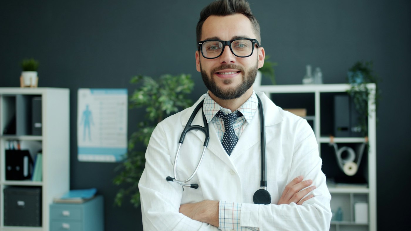 Médico con estetoscopio de brazos cruzados en su consulta