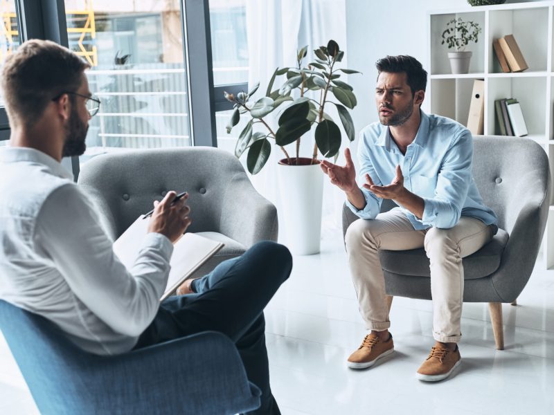 Trying to help. Young frustrated man speaking and gesturing while sitting on the therapy session with psychologist