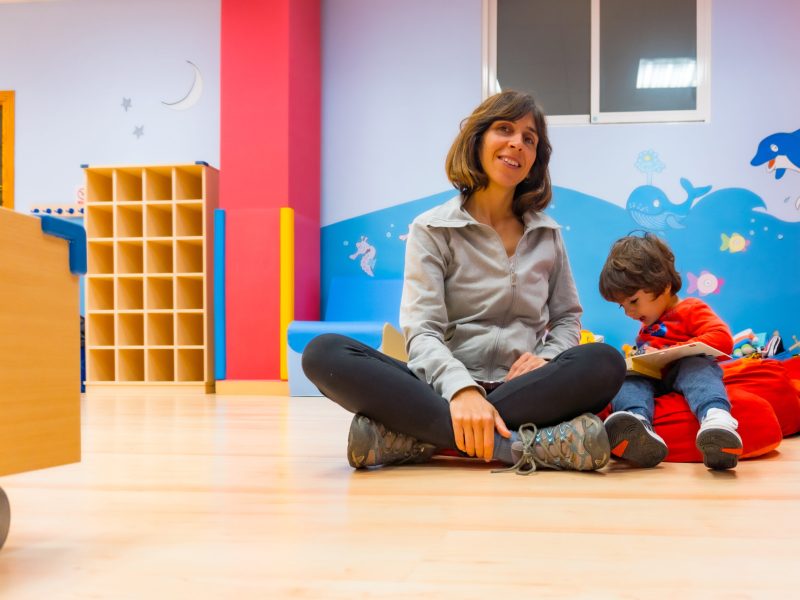 Portrait of a female teacher with a child sitting reading a story book, indoor of a kindergarten